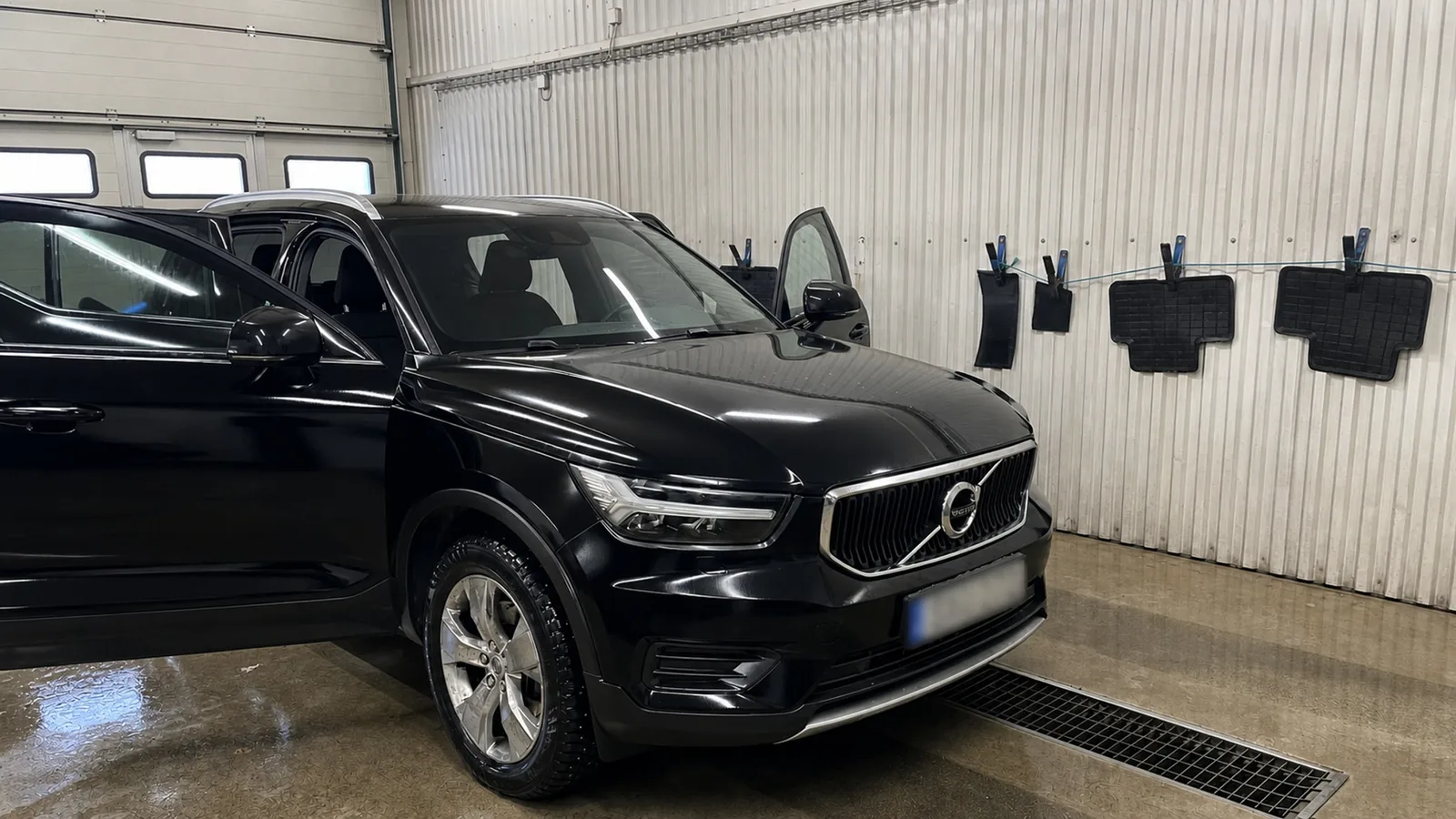 Svart Volvo XC40 efter rekond med nytvättade gummimattor på tork i bakgrunden